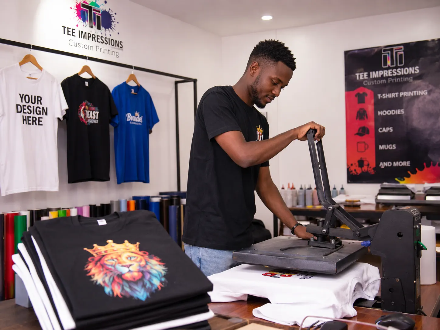 Young man using a heat press to print designs on t-shirts in a custom apparel printing shop